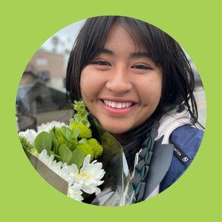 Student with graduation grown holding white and green flowers